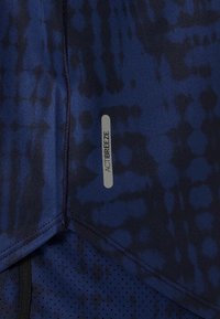 Gros plan sur un tissu à motifs bleu et noir avec une couture noire et une étiquette "ACTIBREEZE" sur un matériau de vêtements de sport.