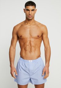 Shorts en coton bleu clair avec une ceinture élastique et une ouverture frontale, présentant un tissu texturé et une étiquette sur la ceinture.