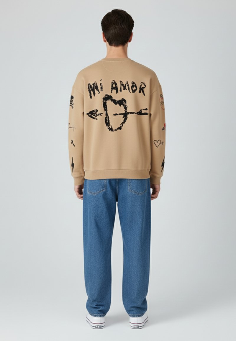 Sweatshirt beige surdimensionné avec des textes graphiques et des motifs noirs au dos. Associé à un jean en denim bleu ample et des chaussures blanches.