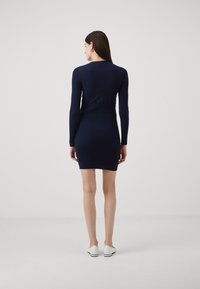 Marineblauwe geribbelde gebreide jurk met lange mouwen, aansluitende silhouet en ronde halslijn. Draagt met witte schoenen. Geen zichtbare patronen of hardware-details.