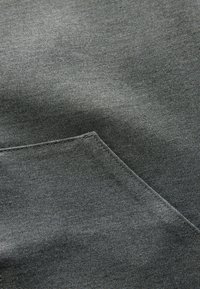 Gros plan sur un tissu gris foncé montrant une texture détaillée et un coin de poche soigneusement cousu.