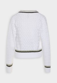 Vit stickad tröja med ett texturerat mönster. Har gröna och svarta randiga detaljer på kragen och nederkanten. Korta ärmar och cropped passform.