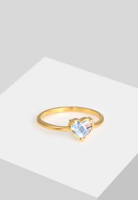 Guld ring med en delikat ring, der har en hjerteformet, facetteret krystal i nuancer af blå og klar, sat i en prongmount.