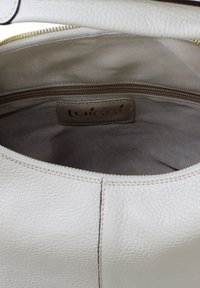 Ljusbeige läderhandväska inuti med en slät textur. Har en hellåst ficka med kontrasterande sömmar och ett tygfoder.