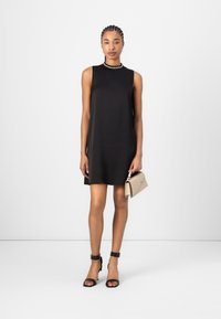 Black sleeveless dress with a smooth texture, paired with black high-heeled sandals and a beige handbag featuring a silver accent.