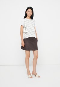 Top corto bianco a maniche corte con motivo stampato, abbinato a una mini gonna in suede marrone scuro e sandali con tacco beige chiaro. Piccola borsa bianca.