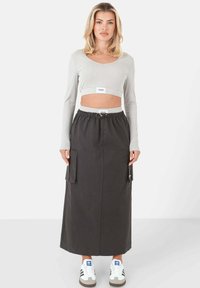 Grijze lange mouwen cropped top gecombineerd met een zwarte cargo rok met zijzakken, een elastische tailleband en gedragen met witte sneakers.