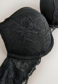 Reggiseno in pizzo nero con coppe preformate, caratterizzato da motivi floreali e bordi scallop. Il tessuto combina pizzo e materiali opachi.