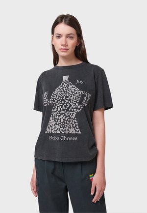 Grå kortærmet t-shirt med en tekstureret hvid grafik af en teapot og teksten "Joy Bobo Choses" trykt nedenfor. Løs pasform.