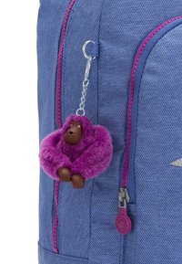 Blå tygryggsäck med en rosa dragkedja och en fluffig lila gorillanyckelring fäst vid den. Nyckelringen har bruna detaljer och en kraftig textur.