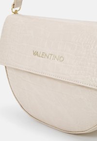 Beige kabelka Valentino z koženky s kroko vzorem, se zlatým logem a krátkým popruhem připevněným zlatými kroužky.