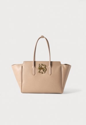 Beige leren handtas met twee hengsels en een goudkleurig decoratief embleem met verstrengelde slangen aan de voorkant.