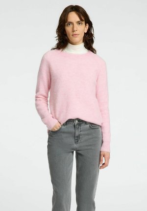 Lys rosa strikket sweater med en rund halsudskæring og ribbede ærmer, parret med grå højdelte jeans. Blød tekstur, afslappet pasform.