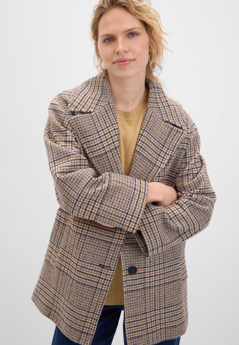 Brun rutigt jacka med överdimensionerad passform, noterade slag och två knappar. Tyget har en texturerad väv och kontrasterande blå och gula linjer.