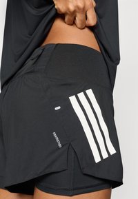 Čierne športové šortky s priedušnou textúrou, vybavené bielymi vertikálnymi pruhmi, bočnými rozparkami a zosilneným pásom.