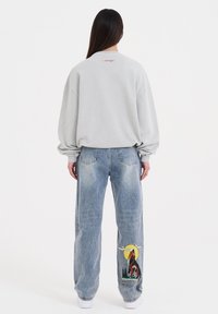 Lichtgrijze oversized sweatshirt met verlaagde schouders en een klein logo op de achterkant, gecombineerd met blauwe vintage-stijl jeans met een wolfgraphic.