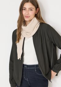 Czarna lekka kurtka bombowiec z białymi akcentami, noszona na białej bluzce, zestawiona z beżowym szalikiem i ciemnoniebieskimi dżinsami.