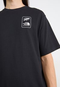 T-shirt en coton noir à manches courtes, avec un patch logo blanc en haut à gauche. Design classique à col rond.