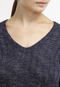 Marineblauwe gebreide trui met V-hals en een gemêleerd, verticaal ribbelpatroon. De stof heeft een zachte, licht glanzende afwerking.