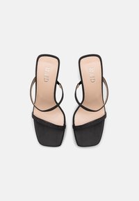 Sandalias negras de punta cuadrada con finas correas en el tobillo y en los dedos, plantillas beige y el nombre de la marca "RAID" impreso dentro de cada zapato.