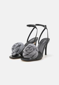 Sorte hælede sandaler med delikate perlebesatte rosemotiver. Har en enkelt rem med ankelspænde og en slank mat finish.