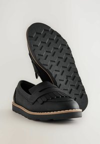 Sorte slip-on sko med en tekstureret overdel, frynsedetaljer og en gummisål med et zigzag mønster og beige accenter.