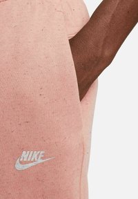 Pink Nike sweatpants feature a soft, textured fabric with a subtle speckled pattern. The logo is displayed in white on the left thigh.