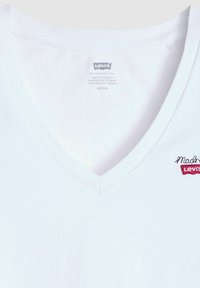 Camiseta blanca de algodón con cuello en V que presenta un pequeño logo bordado de Levi's en rojo en el lado izquierdo, con una textura suave y un diseño minimalista.