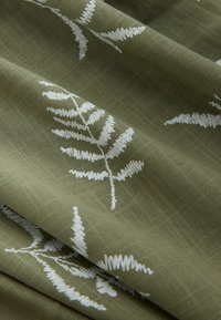 Tissu vert avec une texture subtile en quadrillage, présentant des motifs de feuilles de fougère blanches brodées dispersées sur la surface.