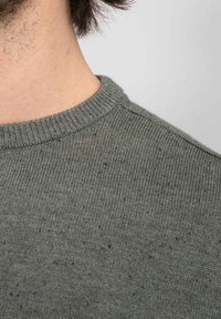 Donkergroene trui met een geribbelde ronde hals, gemaakt van gebreid materiaal met een gespikkelde textuur. Close-up van het schoudergebied.