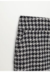 Tissu pied-de-poule noir et blanc en gros plan montrant un motif tissé texturé sur une pièce rectangulaire pliée sur un fond uni.