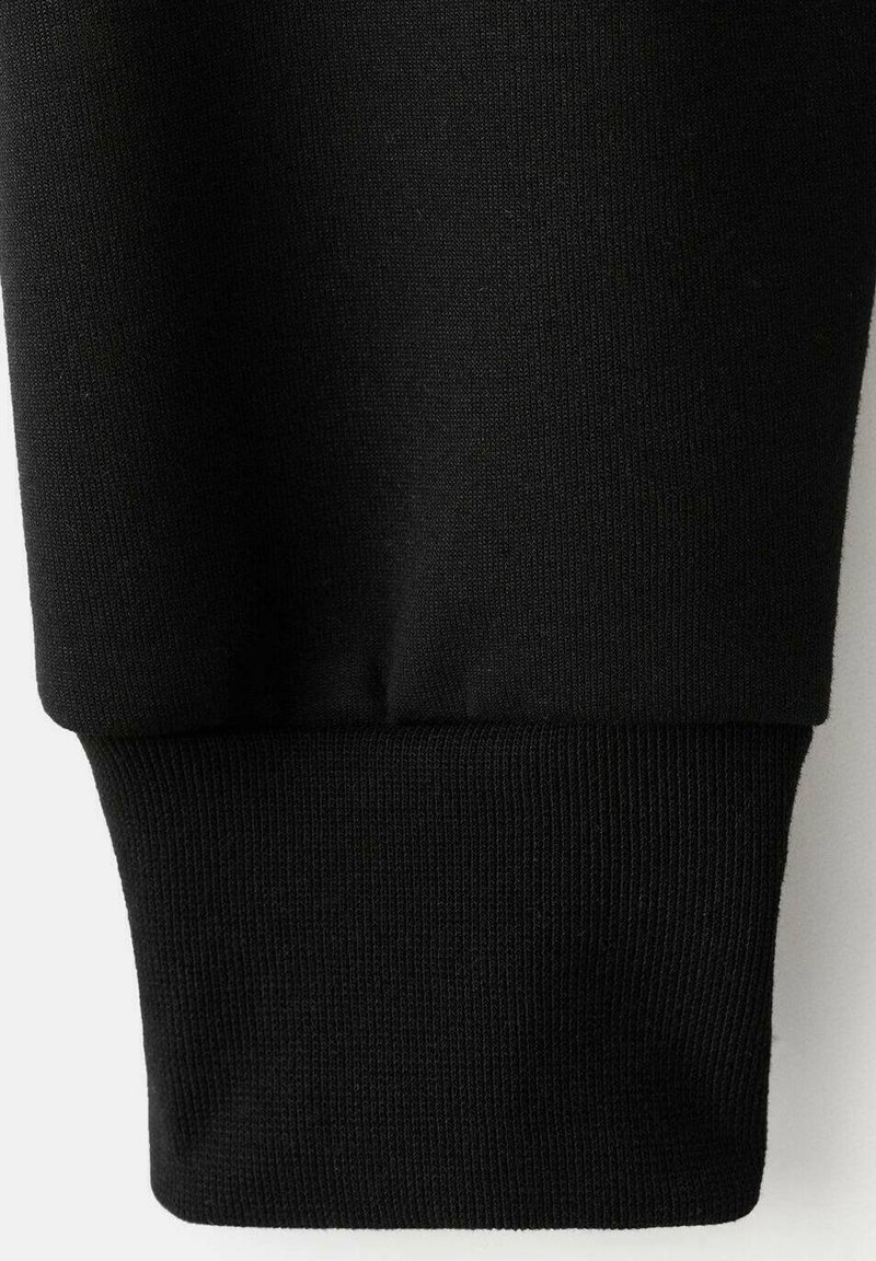 Puño de sudadera de algodón negro con textura acanalada. Presenta un ajuste ceñido y elástico, y un acabado de tela suave.