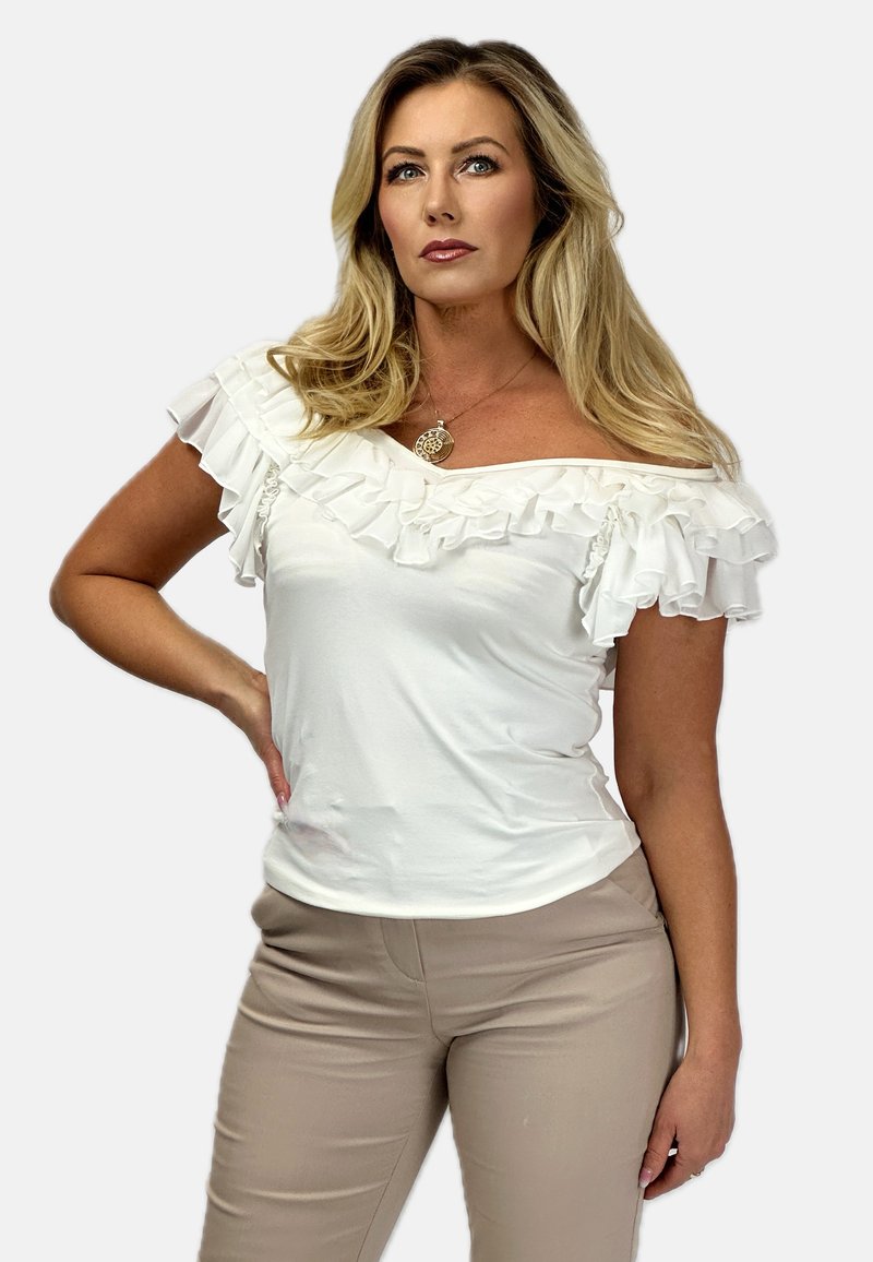 Biała bluzka hiszpanka z falbanami, wykonana z gładkiego materiału. Połączona z dopasowanymi beżowymi spodniami, podkreślającymi smukłą sylwetkę.