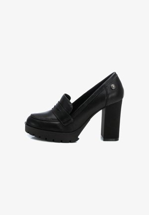 Mocasín negro de tacón alto con parte superior de cuero liso, puntera redondeada y tacón grueso. Presenta una correa decorativa y suela texturizada.