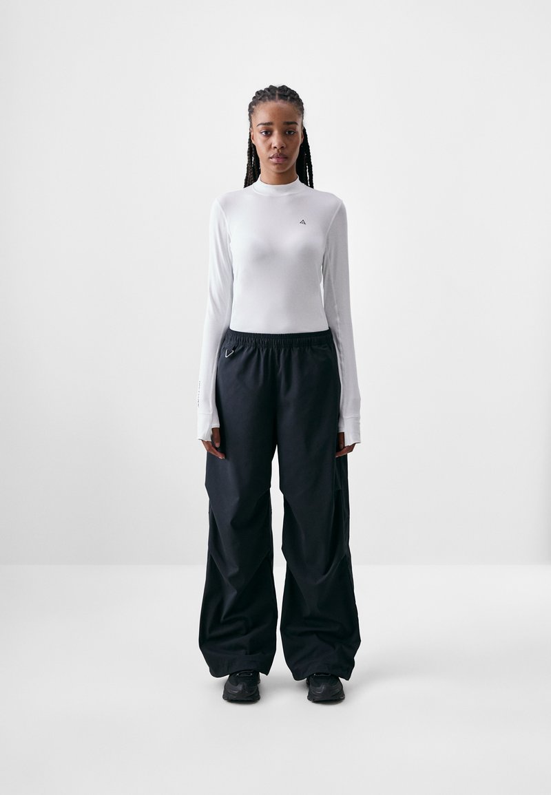 Long-sleeve white top with logo detail and thumbholes, paired with loose-fitting black pants featuring an elastic waistband and accent hardware.