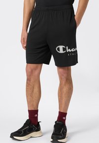 Czarne spodenki sportowe z elastycznym pasem, z białym logo oraz gładk�ą, lekką teksturą materiału.