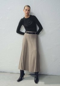 Črna majica z dolgimi rokavi iz teksturirane tkanine, kombinirana z visokim bež plisiranim krilom ter črnimi dolgimi škornji z visoko peto.