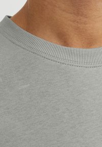 Suéter de cuello redondo de algodón gris con cuello acanalado, textura suave y sutiles variaciones en la superficie de la tela. Vista en primer plano.