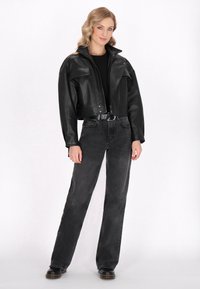 Zwarte, cropped leren jas met een hoge kraag en twee voorkeurszakken, gedragen over een zwarte top en gecombineerd met donkergrijze jeans en zwarte laarzen.