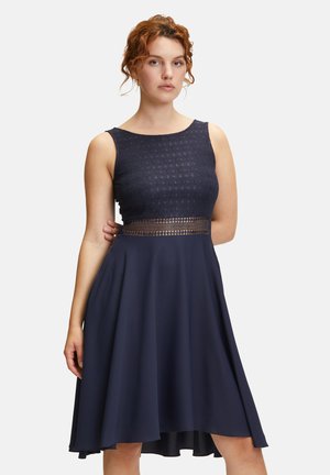 Navyblaues Kleid mit strukturiertem Oberteil und Ausschnitt in der Taille, ausgestattet mit einem ausgestellten Rock, der bis zur Mitte der Wade reicht.