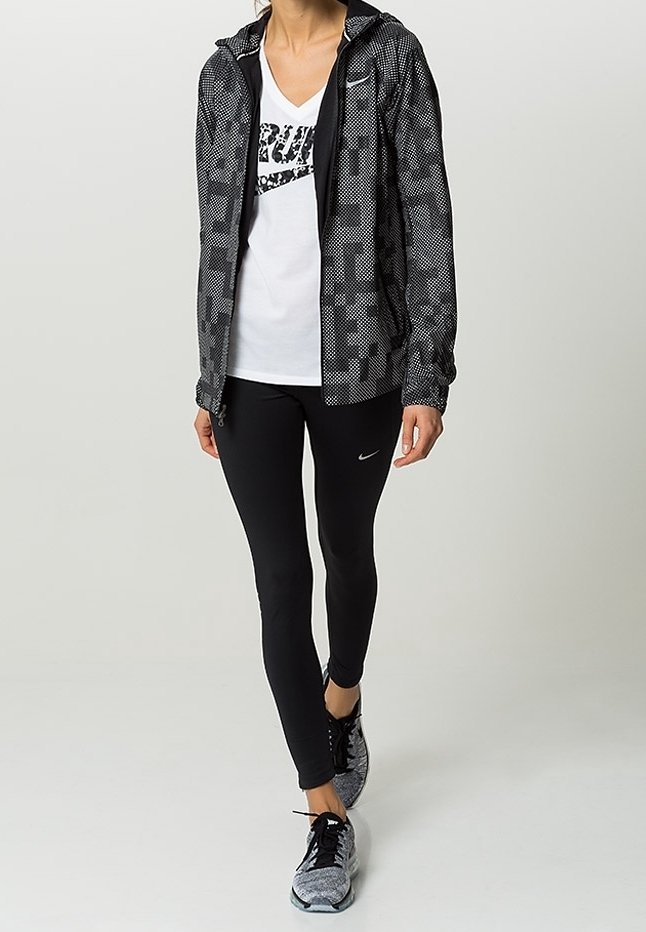 Ensemble de sport Nike noir et blanc, comprenant une veste zippée à motif, un T-shirt blanc avec logo, un legging noir et des baskets grises.