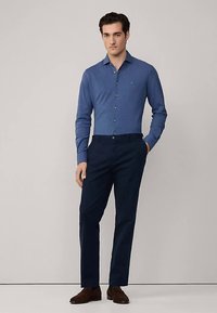 Světlomodrá košile s dlouhým rukávem a límcem na knoflíky, doplněná tmavě modrými kalhotami. Košile má jemnou strukturu a střih.