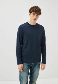 Maglietta a maniche lunghe blu navy con colletto tondo, realizzata in tessuto morbido, abbinata a jeans blu in una vestibilità casual. Design semplice senza motivi.
