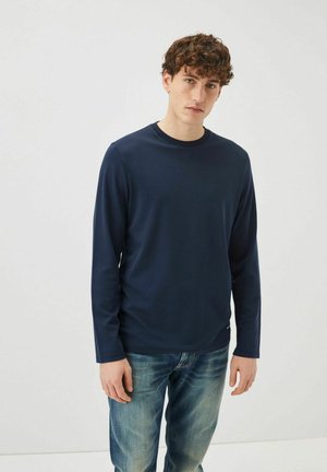 Maglietta a maniche lunghe blu navy con colletto tondo, realizzata in tessuto morbido, abbinata a jeans blu in una vestibilità casual. Design semplice senza motivi.