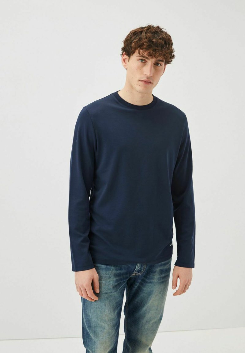 Maglietta a maniche lunghe blu navy con colletto tondo, realizzata in tessuto morbido, abbinata a jeans blu in una vestibilità casual. Design semplice senza motivi.