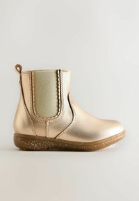 Botín metálico dorado con panel lateral elástico, bordes ondulados y suela marrón moteada. Pequeño lazo en la parte trasera para facilitar el calzado.