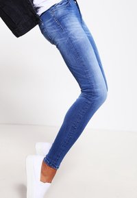 Jeans de denim azul ajustados con un lavado desgastado, que cuentan con cinco bolsillos, una cremallera en la bragueta y un ajuste ceñido en las piernas.