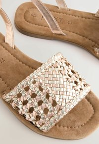 Braune Wildledersandalen mit einem breiten, geflochtenen Riemen mit metallischen Akzenten, flacher Sohle und minimalistischer Design. Offene Zehen.