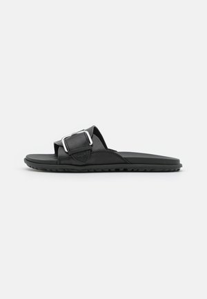 Zwarte slides sandal met een gestructureerde zool, brede verstelbare band met een grote zilveren gesp en een gevoerd voetbed.