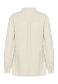 Lyse beige linnedragt med krave, lange ærmer og manchetter med knapper. Har en rygskråning og en lige nederste kant. Blød tekstur.